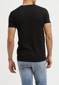 Černé bavlněné tričko s kulatým výstřihem a krátkými rukávy, přiléhavý střih. V kombinaci se světle modrými džíny s detaily šití vzadu.