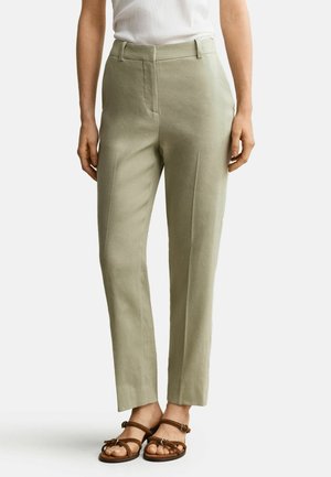 Pantalon vert clair ajusté porté avec des sandales marron à brides et un haut blanc sans manches, montré de la taille aux pieds.