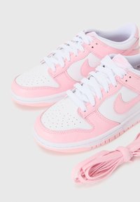 Valkoiset ja vaaleanpunaiset Nike-tennarit, joissa on sileä nahkapinta, rei'itetty varvas ja nauhakiinnitys. Mukana vaaleanpunainen nauha.