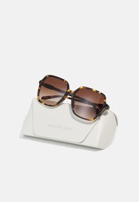 Rudos gradientų saulės akiniai su vėžlio kriauklės rėmu, padėti ant balto dėklo, ant kurio įspausta "Michael Kors." Kvadratinė forma, blizgus paviršius.