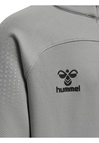 Grå atletisk topp med texturerat tyg, med ett bikakemönster på ärmen och en svart logotyp på bröstet.