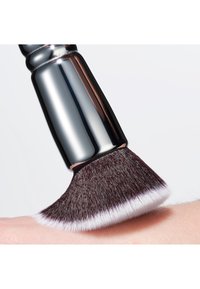 Pennello da trucco rotondo con manico cromato, setole morbide di un bordeaux scuro con punta bianca, appoggiato su una superficie di tonalità della pelle chiara.