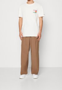 Camiseta de algodón blanca con un gráfico colorido en el pecho, combinada con pantalones de pierna ancha marrones y zapatillas blancas.