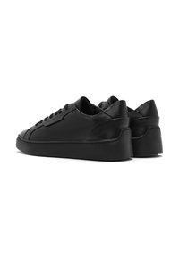 Des sneakers noires en cuir avec une finition lisse, un bout arrondi et une semelle épaisse. Des coutures discrètes ajoutent du détail au design.