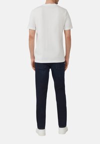 Witte kortekragen t-shirt gezien vanaf de achterkant, met een ronde hals en een gladde stof, gecombineerd met donkerblauwe jeans en witte sneakers.