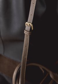 Bracelet en cuir marron réglable avec boucle métallique dorée sur fond sombre, montrant des bords cousus et plusieurs trous.