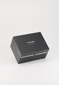 Boîte noire rectangulaire avec une finition texturée, dotée de quincaillerie en argent et du texte "DI MILANO" en blanc sur la surface supérieure.
