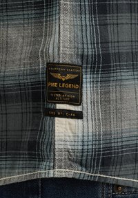 Blauw en grijs geruite stof met een gestructureerde afwerking. Heeft een zwart en gouden label met de tekst "PME LEGEND" en details over hoogte testen.