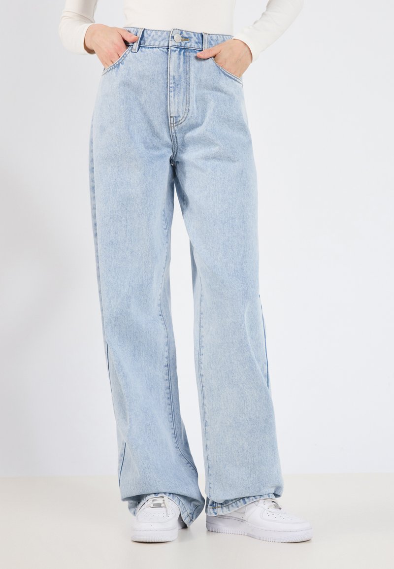 Jean en denim bleu clair avec une taille haute, un design à jambes larges et de légentes fentes sur les côtés. Associé à des baskets blanches, avec une coupe classique.