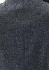 Mørkegråt stof bagside med en glat overflade og en lodret søm, der løber centralt. Materialet ligner et fint væv eller twill.