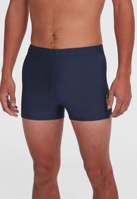 Tamsiai mėlyni maudymosi šortai iš lankstaus audinio, turintys kūną priglundantį dizainą, lygų paviršių ir šone esantį logotipą.