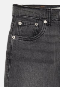 Jeans de mezclilla negra con un diseño clásico de cinco bolsillos, herrajes metálicos y una textura suave con detalles de desvanecimiento sutil.