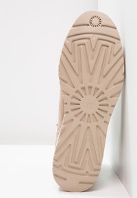 Suela de zapato de color beige claro con un patrón texturizado en zigzag y un logo en forma de sol. Fabricada en goma, presenta un diseño de agarre detallado.