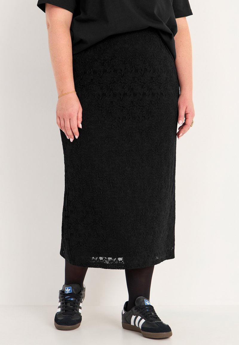 Schwarzer Midirock aus Spitzenstoff mit einem texturierten Blumenmuster. Kombiniert mit schwarzen Sneakers und blickdichten schwarzen Strumpfhosen.