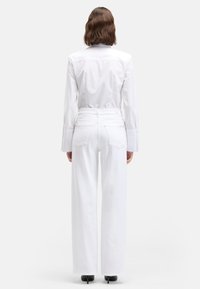 Biała koszula na guziki z długimi rękawami, zestawiona z białymi, wysokim stanem dżinsami o prostych nogawkach i minimalnymi zdobieniami na tylnych kieszeniach.