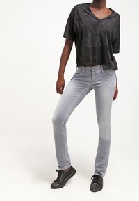 Camiseta negra de manga corta con escote en V, combinada con jeans ajustados de un gris claro y zapatillas negras, con una textura suave y cierre de cinco botones.