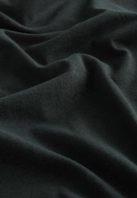 Tessuto di cotone nero con una superficie liscia, che presenta morbide pieghe e un leggero allungamento. Nessun motivo visibile o accenti aggiuntivi.