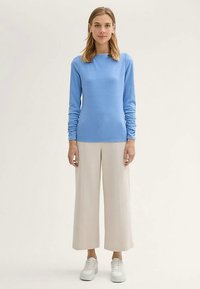 Svetlo modra dolg rokav pulover z oprijeto obliko in nabranim detajlom na rokavih, kombiniran s krem širokimi hlačami in belimi supergami.