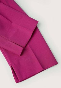 Gros plan d'un tissu magenta vif plié sur un fond clair avec des bords nets visibles et des plis marqués.