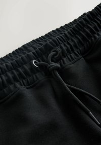 Schwarze Jogginghose mit einem gerippten elastischen Taillenbund und Kordelzug, glatter Textur und dezenten Nähten an den Fronttaschen.