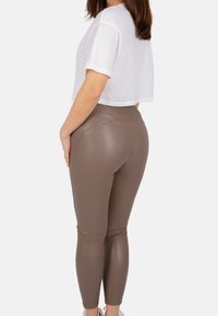 Leggings en simili cuir marron avec une taille haute et un ajustement serré, associées à un t-shirt blanc court, vues de côté.