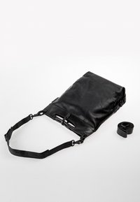 Borsa in pelle nera con una forma piatta e rettangolare. Presenta una tracolla rimovibile, hardware in metallo e un design a apertura superiore. Include una tracolla arrotolata.