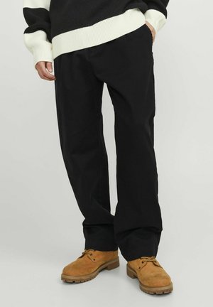Pantaloni in cotone neri con vestibilità ampia, dotati di tasche laterali e una texture liscia, abbinati a stivali marroni con lacci.