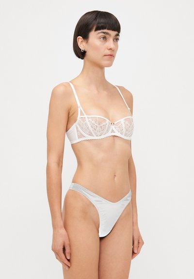 Witte kanten bralette met onderdraad, doorschijnende panelen en verstelbare banden. Gecombineerd met een lichtgrijze satijnen thong met minimale bedekking.
