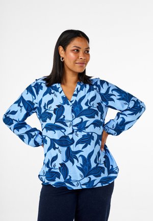 Blouse à imprimé floral bleu avec des manches longues et un décolleté en V. Présente des motifs de feuilles bleu foncé sur un fond bleu clair. Texture de tissu douce.