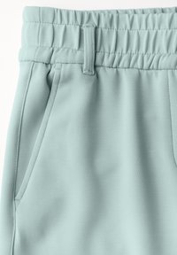 Pantalon de survêtement bleu clair avec une taille élastique, doté d'un cordon de serrage et de poches latérales. Le tissu est lisse avec une finition mate.