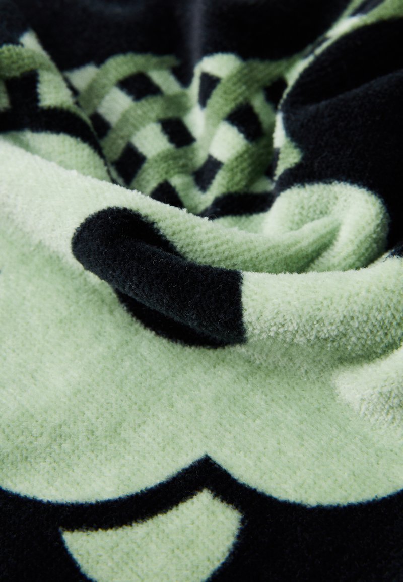 Manta de forro polar en verde pálido y negro, con un patrón de tablero de ajedrez y formas curvas, con un acabado suave y texturizado.