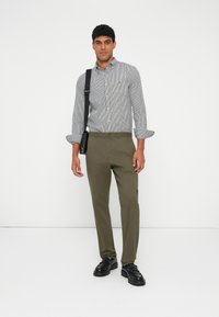 Striped button-up shirt with long sleeves, paired with olive green trousers. Black shoes complete the look, along with a shoulder bag.