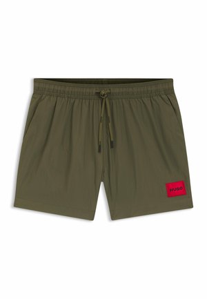 Olive green swim shorts with an elastic waistband, drawstring closure, and a red fabric patch labeled "HUGO" on the lower front.