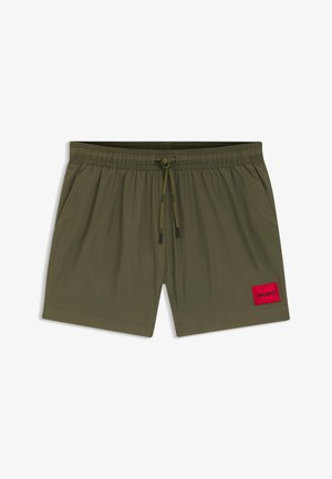 Olive green swim shorts with an elastic waistband, drawstring closure, and a red fabric patch labeled "HUGO" on the lower front.