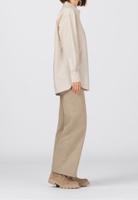 Beige Langarmhemd mit Standardkragen, kombiniert mit lockeren, hellbraunen Hosen und beigen Stiefeln mit rutschfester Sohle.