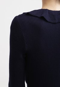 Námořnicky modrý žebrovaný svetr s kulatým límečkem. Textura je hladká s vertikálními žebry, vytvářející přiléhavý střih.