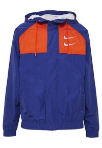 Modrá a oranžová bunda Nike s kapucí, elastickými manžetami a předním zipem. Hladká textura s logem na hrudi.
