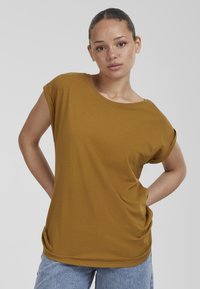Senapsgul t-shirt, mjukt bomullsmaterial, rund halsringning, korta uppvikta ärmar, avslappnad passform, tillsammans med ljusblå denimjeans.