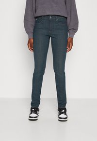 Indigo slim-fit traperice s klasičnim dizajnom s pet džepova, s kopčanjem na gumb, kontrastnim šavovima i mekanim traperom.