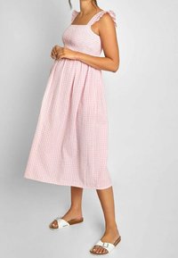 Rosa rutigt midiklänning med fyrkantig halsringning, volangaxlar och smockad livstycke. Bärs med vita sandaletter på en neutral bakgrund.