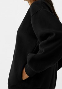 Svart sweatshirt med avslappnad passform, ribbade muddar och nederkant, samt sidofickor. Mjuk tygtextur som visar upp en minimalistisk design.