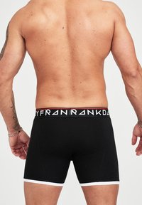 Schwarze Boxershorts mit einem weißen Saum und einem elastischen, markierten Bund, der ein Logo in kontrastierenden Farben aufweist. Glatter, dehnbarer Stoff.