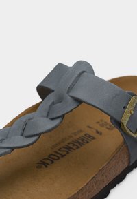 Κοντινή λήψη μπλε σουέτ πλεγμένης λουρίδας με χρυσή αγκράφα σε σανδάλι με πάτο φελλού που δείχνει τη σήμανση Birkenstock.