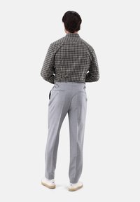 Karierte Hemd in Dunkelgrün und Weiß, kombiniert mit hellgrauen Hosen und weißen Sneakers. Sichtbare Details der hinteren Taschen und verstellbarer Bund.