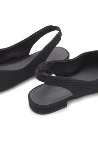 Zapatos negros tipo slingback con parte superior de tejido texturizado, suela plana y diseño minimalista con forro interior suave y sin adornos.