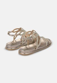 Metallic gouden sandalen met ingewikkeld uitgesneden banden, versierd met heldere rhinestones, en een platte zool met een lichte hak.