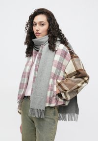 Halli sall ääreliinidega, mis on heidetud üle ruudulise jaki, millel on roosa, pruun ja kreemikas värv. Kanditud heleroosa topi ja roheliste teksade peal.