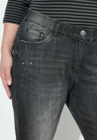 Černé džíny z denimu s mírně vybledlým vzhledem. Obsahují jemné ozdoby na stehně a klasický design se pěti kapsami.