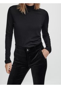 Sort turtleneck med lange ærmer parret med højtaljede bukser i sort velour, der har en frontlomme og knaplukning.