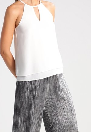 Weißes ärmelloses Neckholder-Top mit vorderem Keyhole, kombiniert mit silbernen metallic plissierten Hosen mit weitem Bein an einer Person.